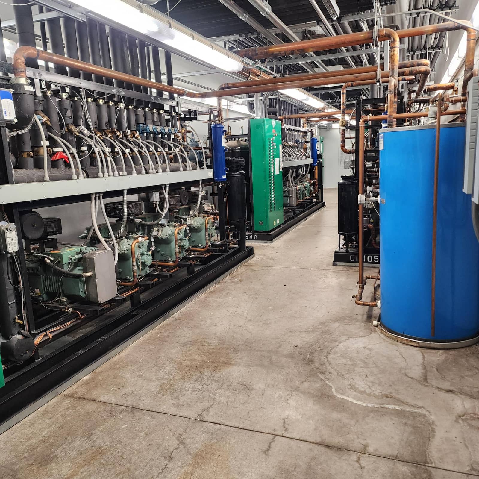 Commercial refrigeration machine room with parallel compressor racks, copper piping, and receiver tanks
