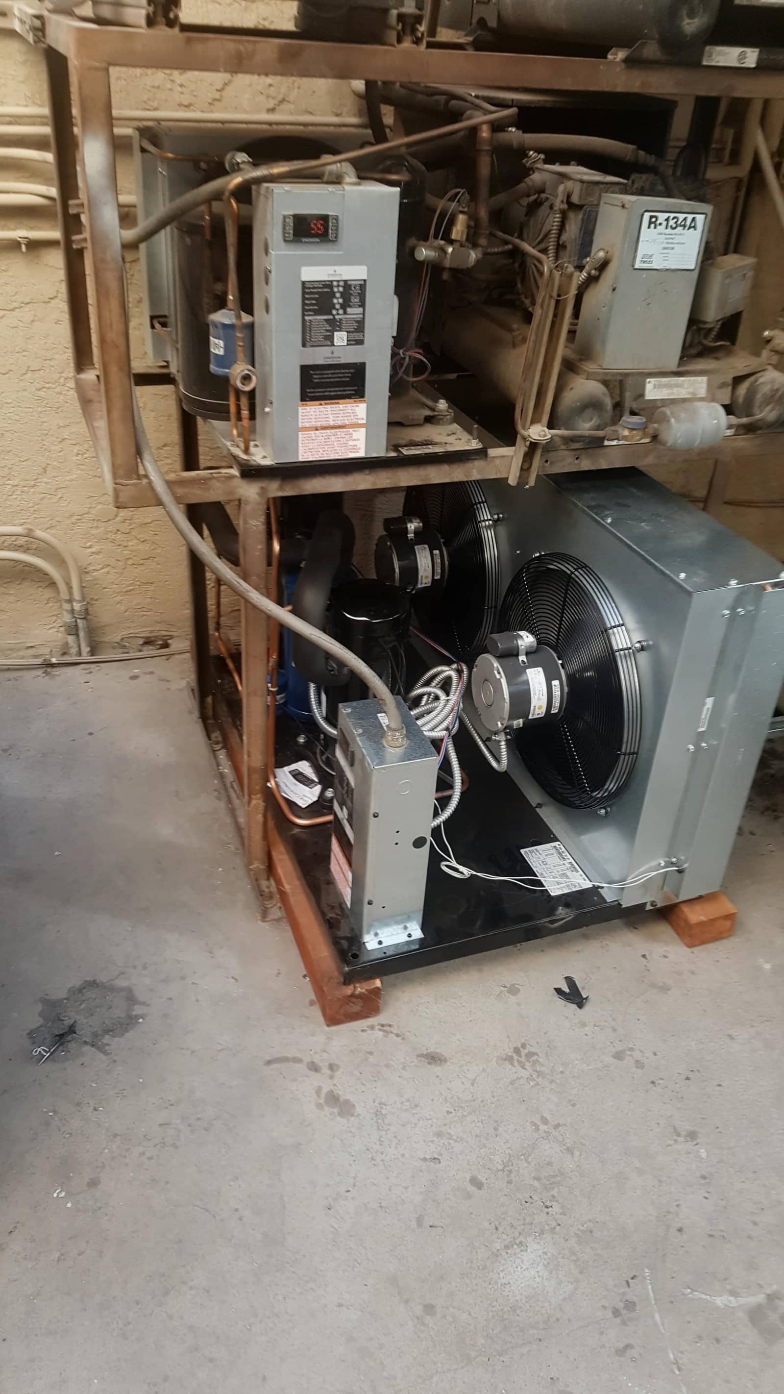 Commercial R-134A condensing unit on a steel rack with compressor, condenser fan, and digital controller during service