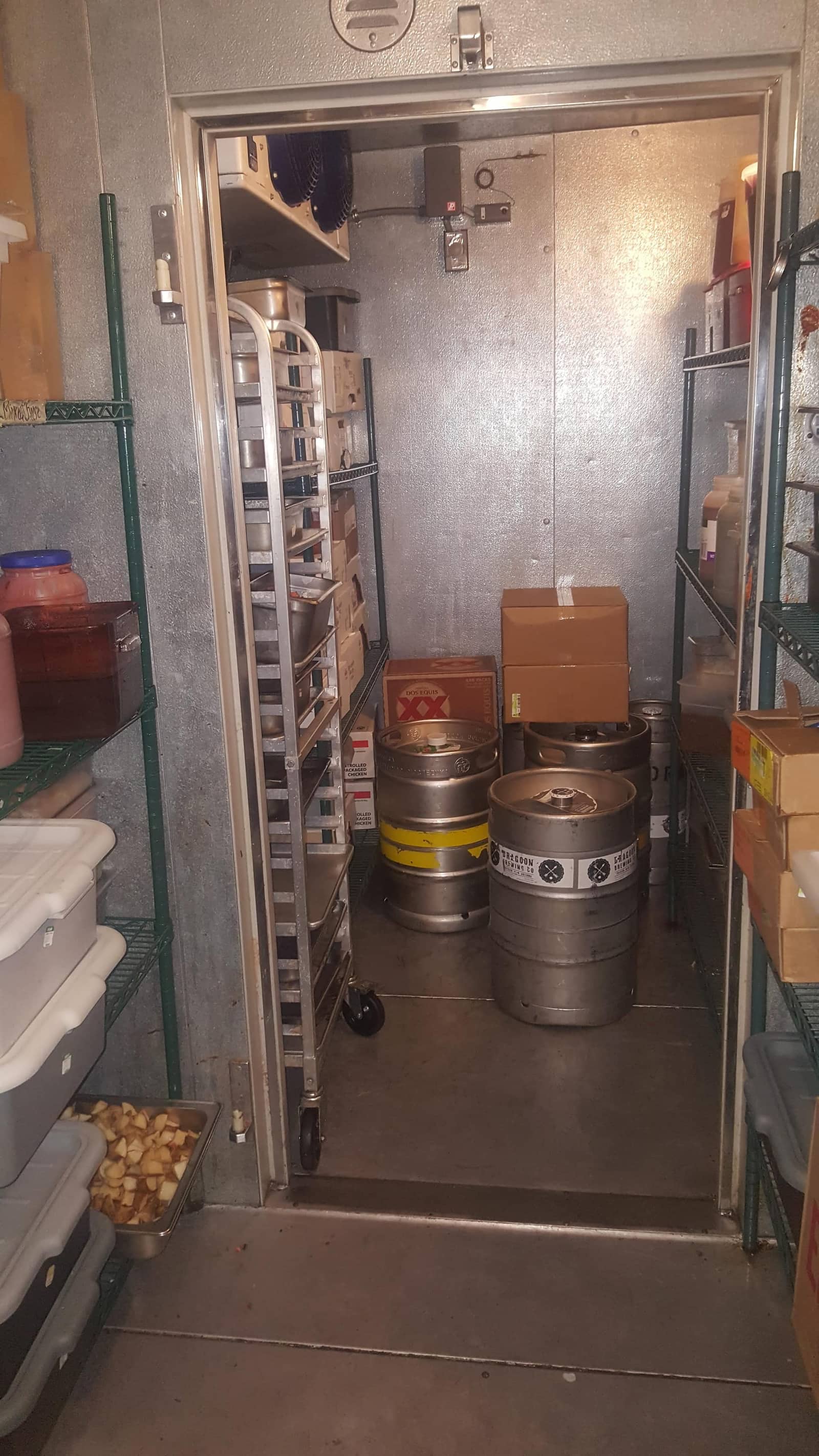 Restaurant walk-in cooler interior with evaporator unit, sheet-pan racks, kegs, and wire storage shelving